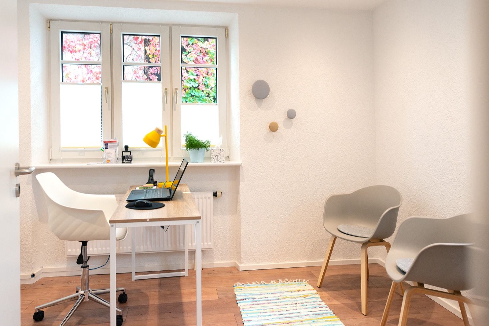 Helles Sprechzimmer mit einem Schreibtisch, Laptop und Stühlen
