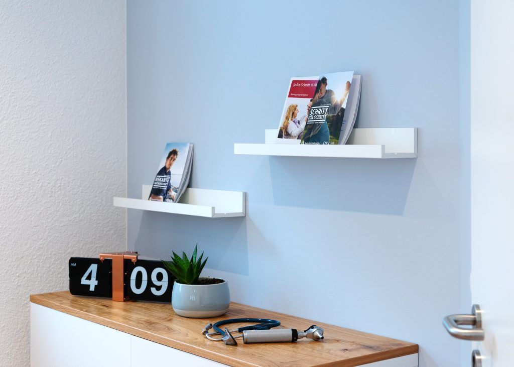 Detailansicht eines Regals mit Fachbüchern und einer Retro-Uhr vor blauer Wand