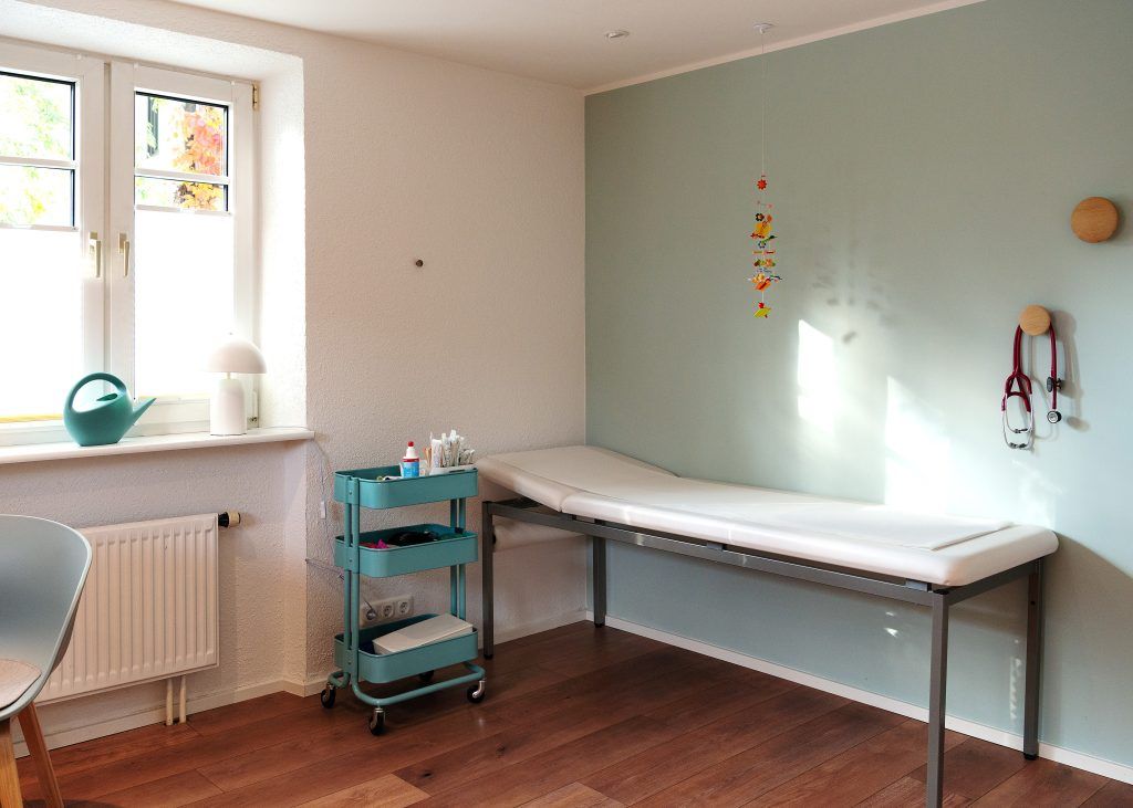 Helles Untersuchungszimmer mit einer Untersuchungsliege und medizinischem Zubehör