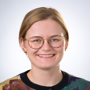 Porträt von Isabel Brand, lächelnd mit Brille und blonden Haaren in einem bunten Oberteil
