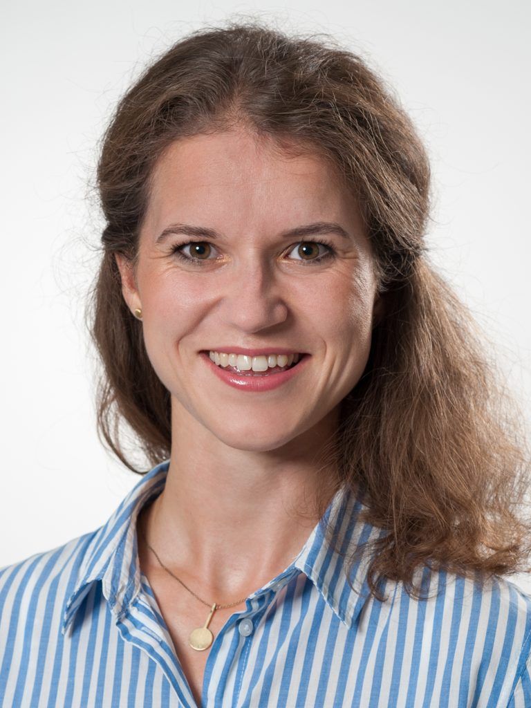 Porträt von Dr. med. Katharina Ertl, lächelnd in einem blau-weiß gestreiften Hemd