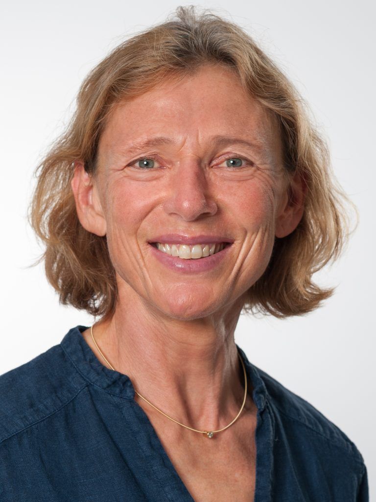 Porträt von Petra Vogel, lächelnd mit kurzen braunen Haaren in einem dunkelblauen Hemd