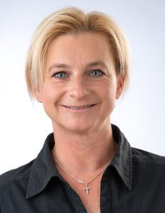 Porträt von Stephanie Hainz, lächelnd mit kurzen blonden Haaren in einer schwarzen Bluse